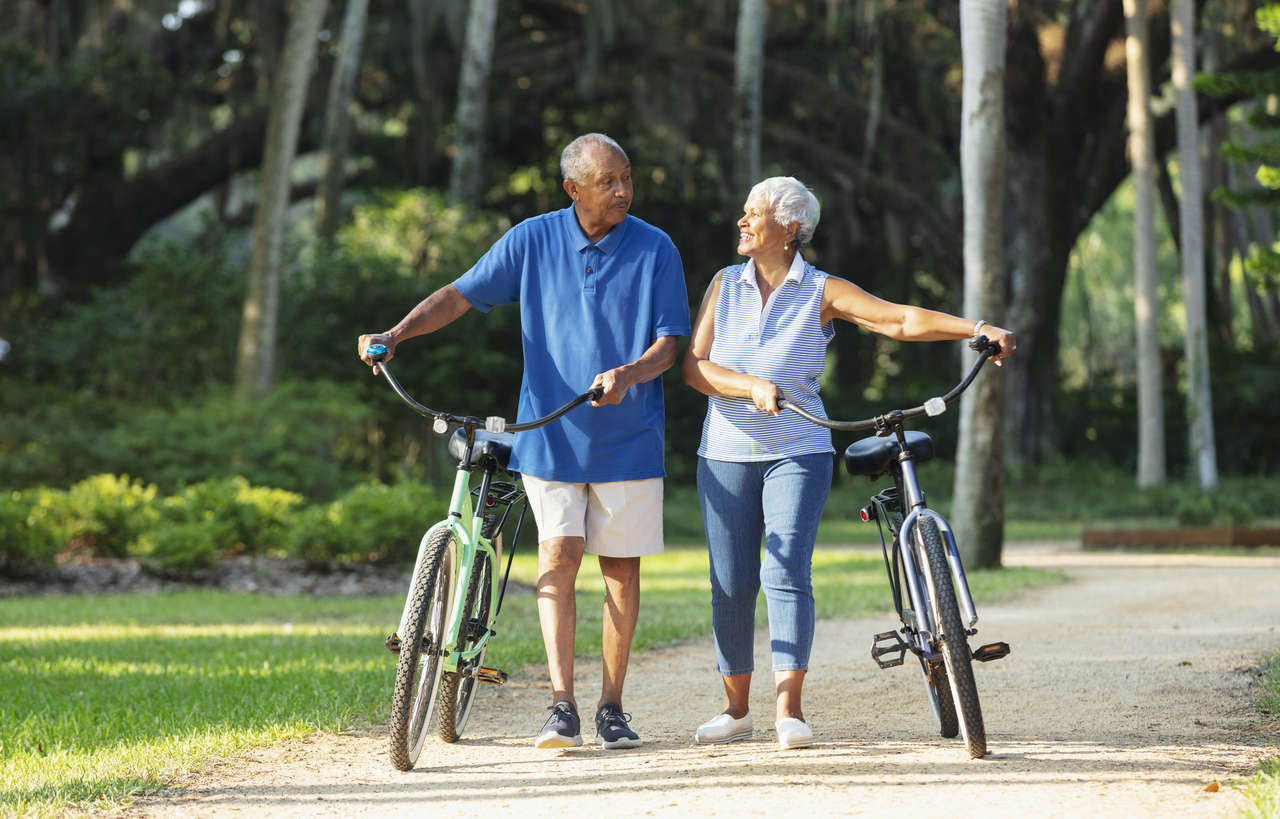 Smiling older couple at the park with bikes, enjoying activities without pain