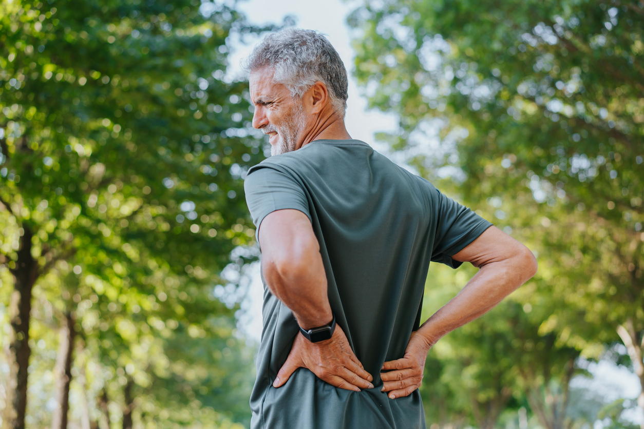 Person in wooded area grasps lower back with both hands in pain