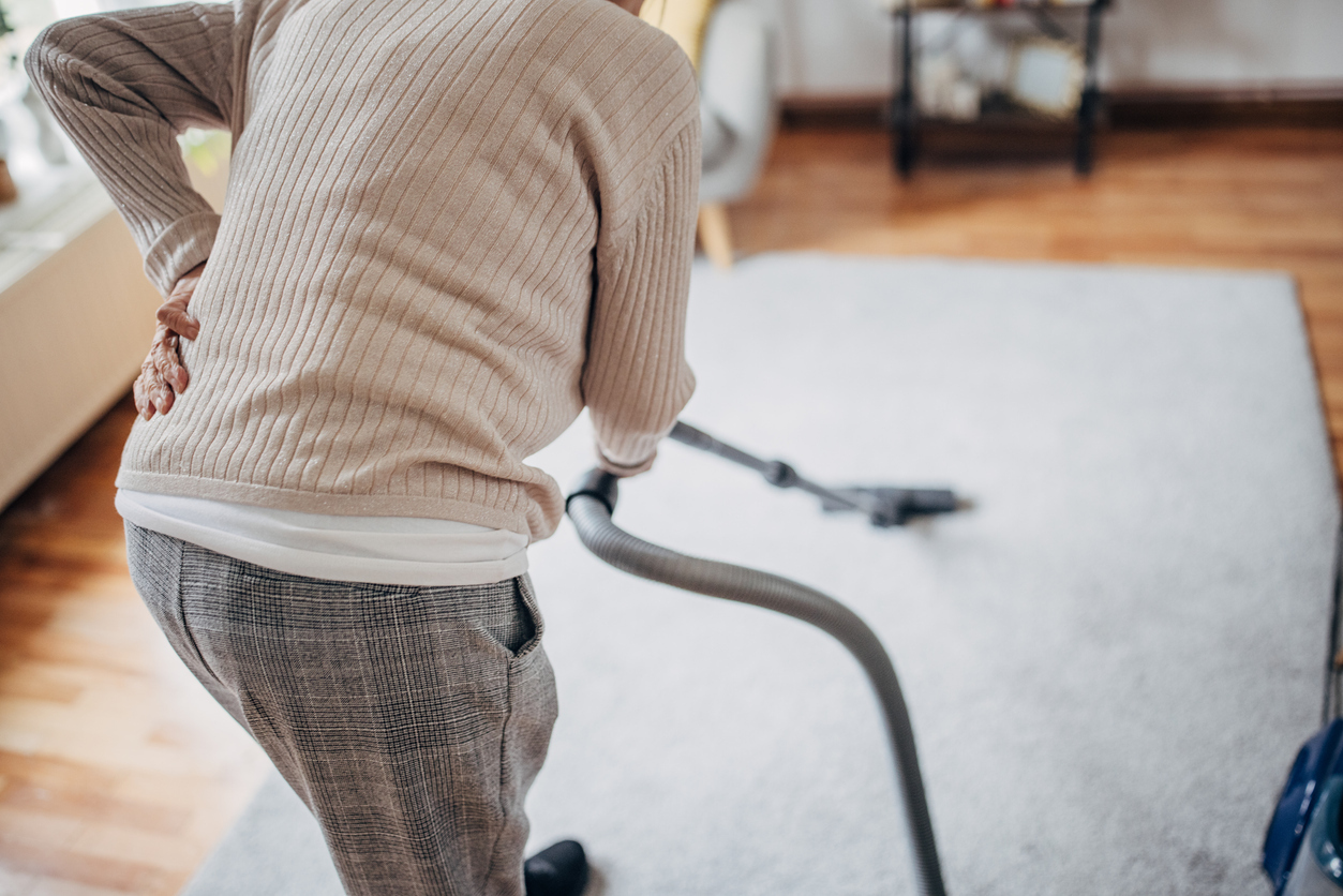Person places hand to back in pain while vacuuming at home