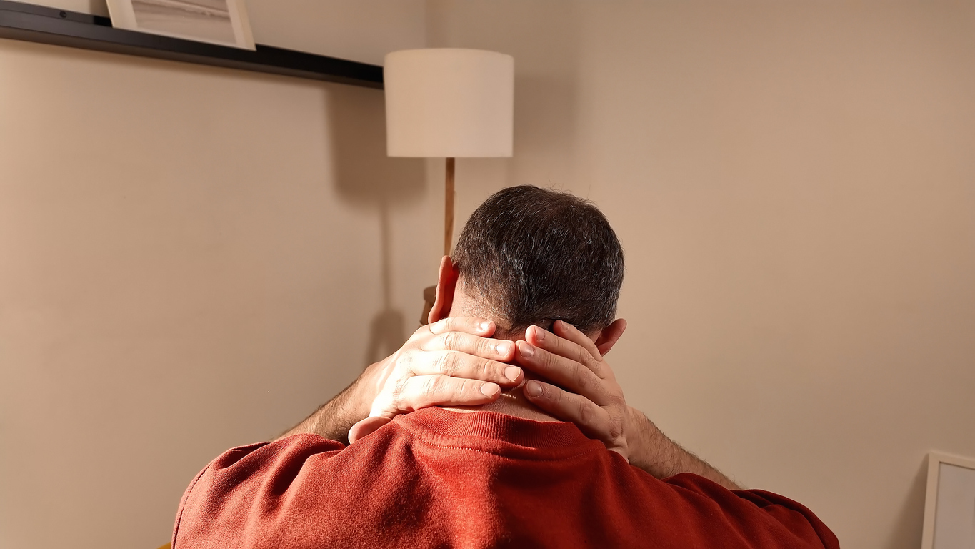 Patient wearing red long-sleeve shirt, sitting and holding back of neck