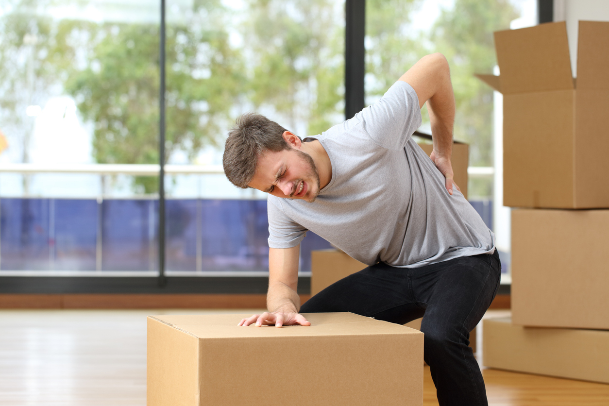 Person experiences back pain while moving boxes