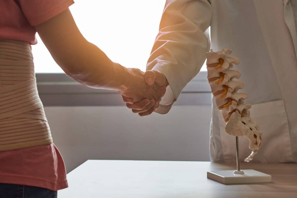 Patient shaking spine surgeon’s hand in medical office