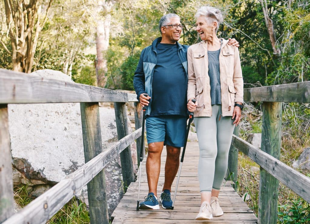Happy senior couple crossing wooden bridge on hike