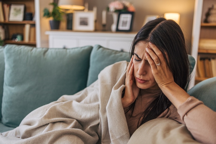 Young person with headache lying on sofa at home