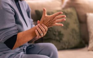 Older person holding painful arm while on couch at home