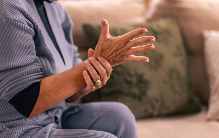 Older person holding painful arm while on couch at home