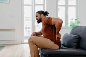 Person sitting on couch holding lower back in pain