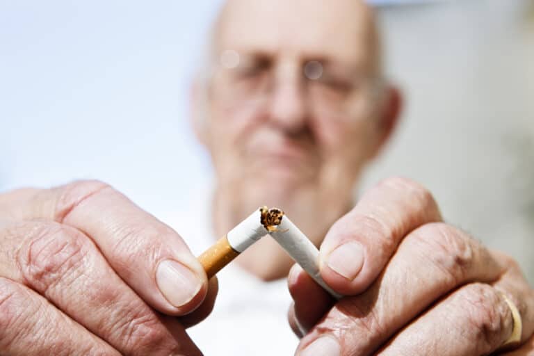 Older individual breaking cigarette in half
