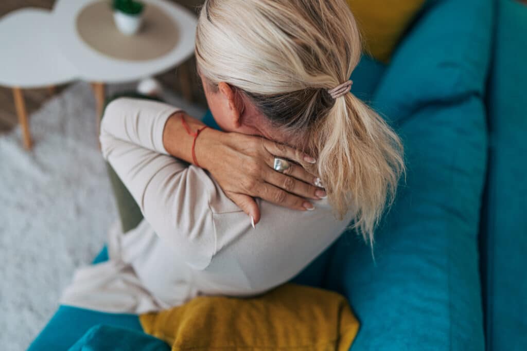 Woman holding painful neck while sitting at home