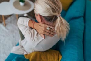 Woman holding painful neck while sitting at home